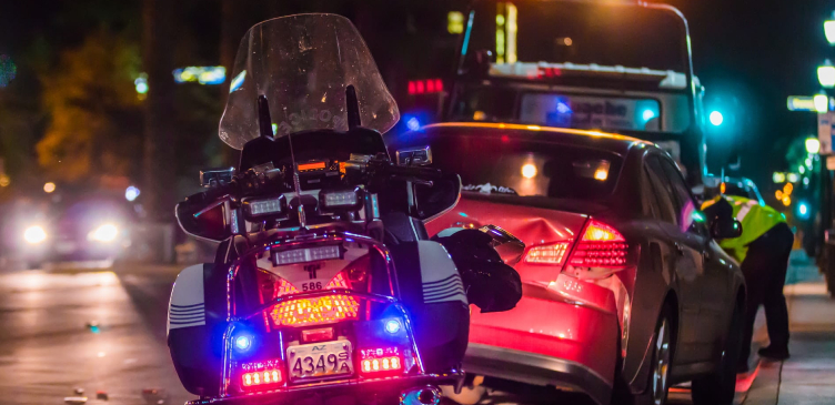 An accident scene, damaged car and traffic poice bike with lights on.