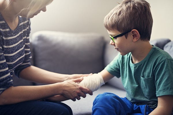 A mother sitting on a couch and tending to her sons wounded arm